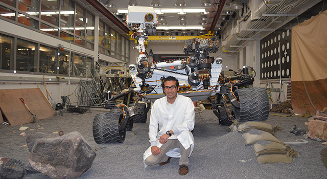 Payam Banazadeh poses with the Engineering Design Unit test-model of the Curiosity rover