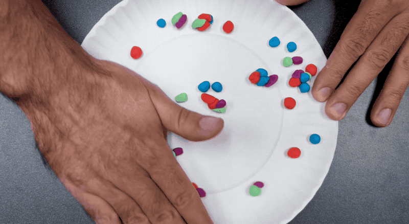 A person moves their hand over different color pieces of playdough on a plate.