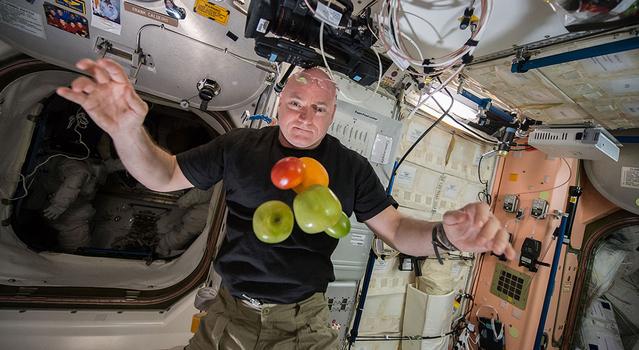 An astronaut poses with a bunch of fruit floating in front of him on the International Space Station