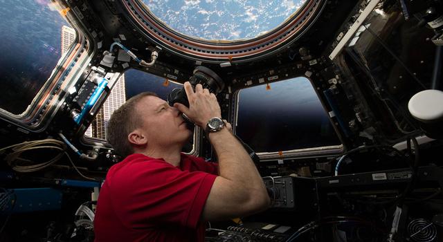 An astronaut points a camera at view of Earth from the window of the International Space Station.