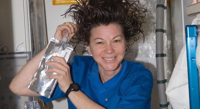 An astronaut holds a pouch of water and squeezes it into her hair to shower on the International Space Station.