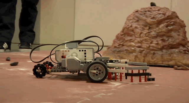 A student-made rover drives across a simulated Mars surface.