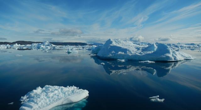 Photo of a body of water covered with icebergs under a blue sky with wispy clouds