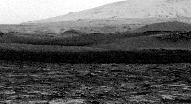 A grainy black-and-white image shows a thin column of dust moving sideways beyond a distant ridge.
