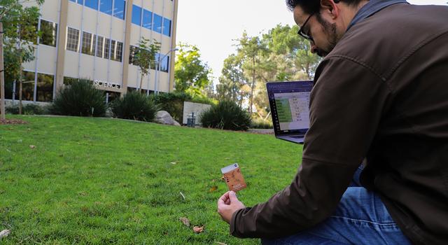 A man kneels down in a grassy field holding a card with a picture of Mars on it.