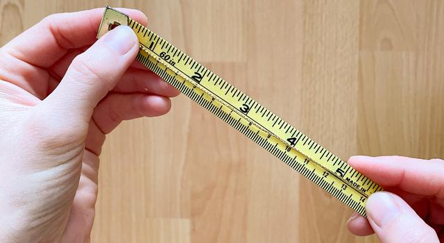 A person holds a gold string across yellow measuring tape