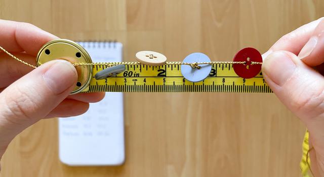 A person holds with buttons of different sizes and colors tied to it across yellow measuring tape