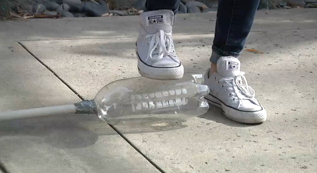 A person's shoe hovers above a empty liter bottle attached to a PVC pipe.