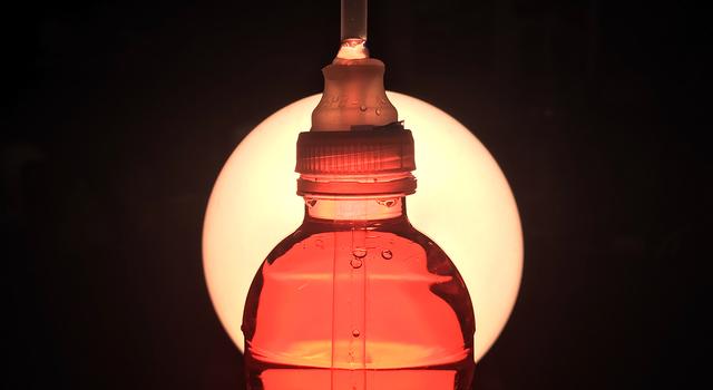 A bright light shines on a water bottle filled with red-colored water
