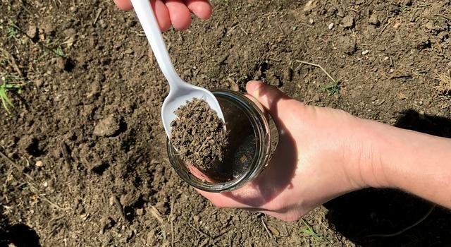 Photo of a person spooning dirt into a jar of water