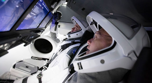 Two astronauts sit in a simulated SpaceX' Crew Dragon spacecraft.