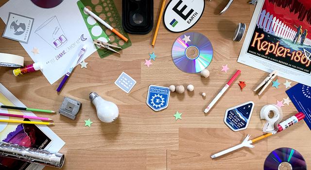 Office supplies, craft materials, space stickers and other objects strewn across a wood floor.