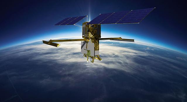A rectangular box-shaped spacecraft with long arms extending from either side. Above the arms are wing-like solar panels extending in the opposite direction. The curvature of Earth and wispy clouds are depicted just below the spacecraft.