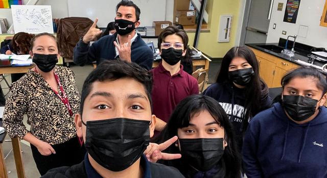 Five students in sweatshirts and collared shirts pose for a selfie with Ms. Risbrough and JPL education specialist Brandon Rodriguez, all wearing masks.